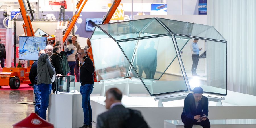 Glaslösungen und Handhabungstechnik auf der glasstec Fachbesucher betrachten eine moderne Glaskonstruktion mit automatisierter Hebe- und Handhabungstechnik auf der glasstec in Düsseldorf