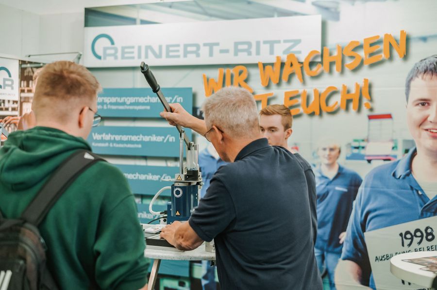 Mitarbeiter demonstriert Jugendlichen eine technische Vorrichtung am Messestand von Reinert-Ritz auf der Arbeitswelten in Nordhorn
