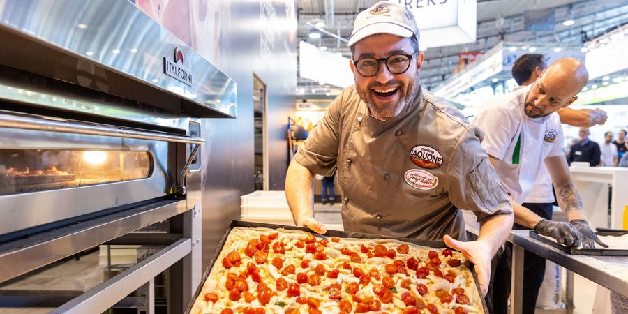 Back- und Snackideen auf der südback Bäcker präsentiert ein frisch gebackenes Blech mit Pizza auf der südback in Stuttgart